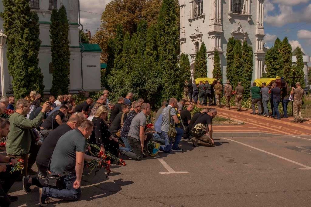 Los dolientes se arrodillan para presentar sus respetos mientras los hombres cargan ataúdes durante el funeral de seis militares ucranianos