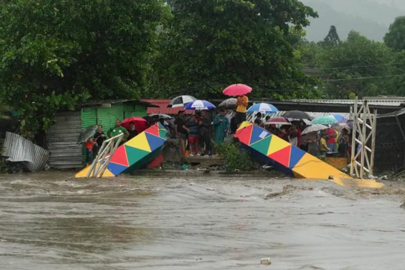 Varias personas paradas frente a un puente peatonal colapsado el sábado 16 de noviembre de 2024 debido a las inundaciones causadas por las lluvias que ha provocado el paso de la tormenta tropical Sara en San Pedro Sula, Honduras.Foto: La Hora/AP