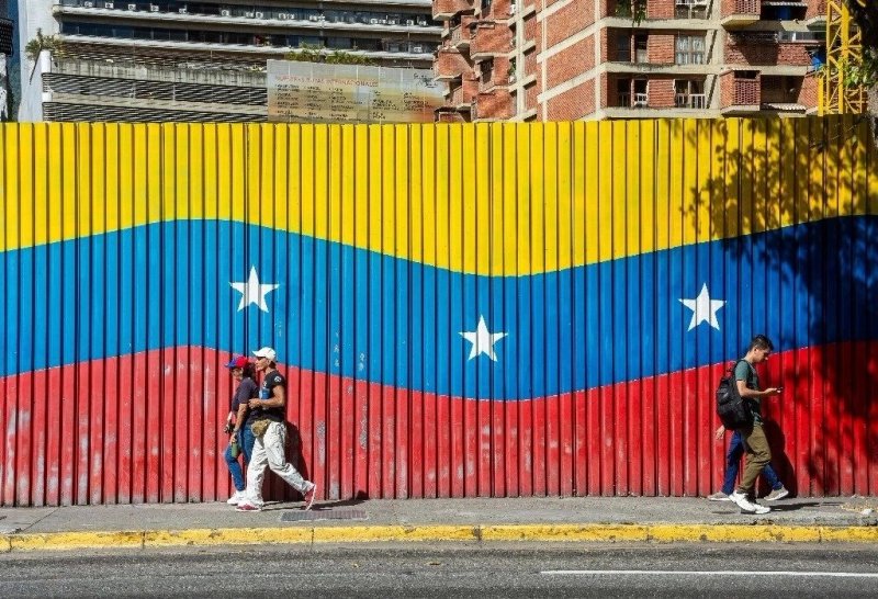 Dos personas caminan delante de una bandera venezolana el 9 de enero de 2025, en Caracas, Venezuela. Foto Europa Press