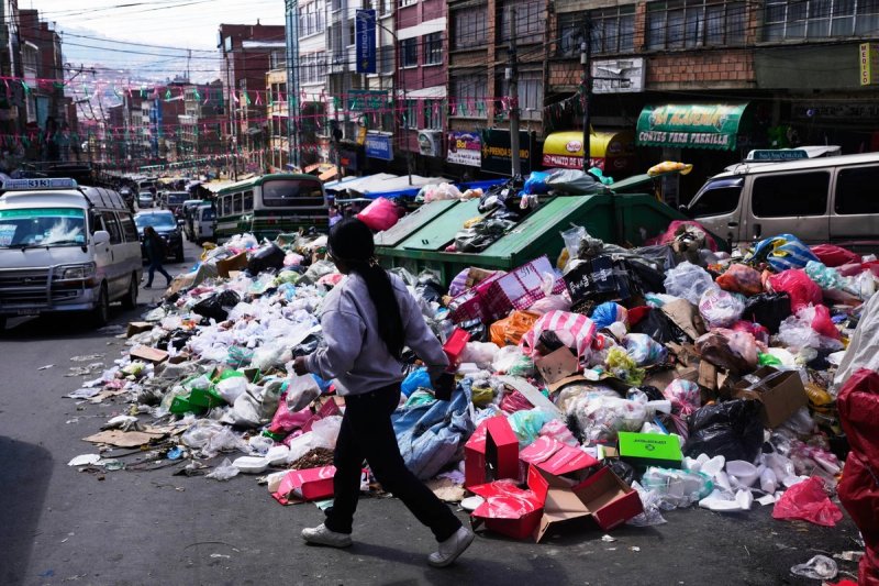Una mujer camina junto a la basura esparcida por la calle durante una huelga de recolectores de basura que exigen mayores tarifas de recolección para compensar el aumento de los costos de combustible y mano de obra en La Paz, Bolivia, el martes 25 de agosto de 2026. Ap