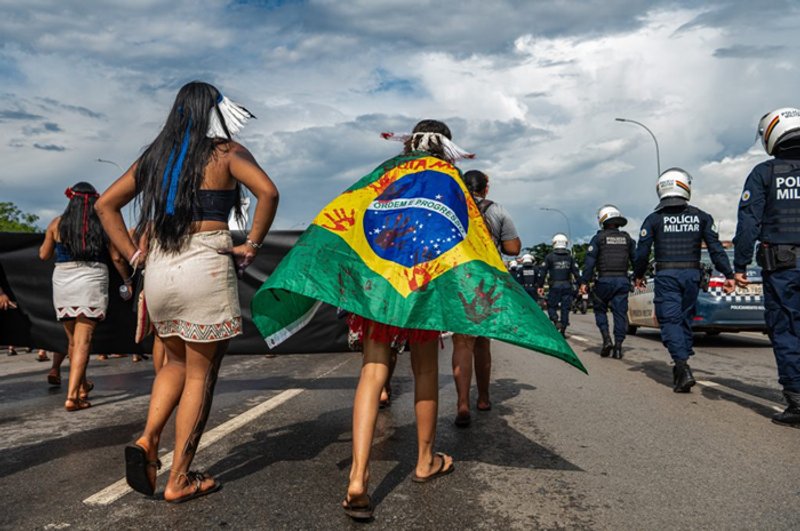 Una manifestante envuelta en una bandera brasileña “ensangrentada” durante una marcha contra los combustibles fósiles en Brasilia, el 9 de abril de 2026. Imagen: Edgar Kanaykõ Xakriabá / Dialogue Earth.
