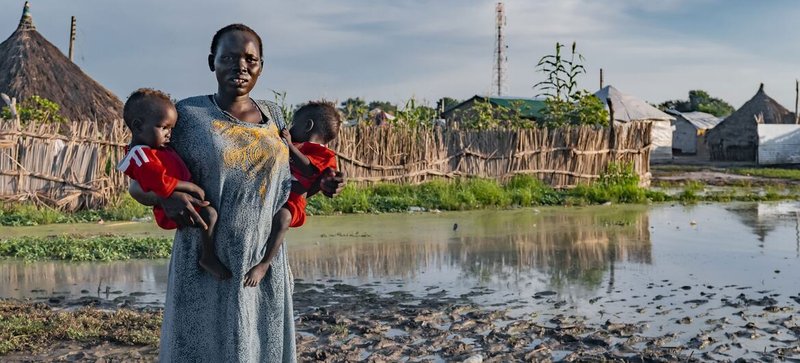© UNICEF Una mujer sostiene a sus hijos frente a su casa afectada por las inundaciones en Sudán del Sur.